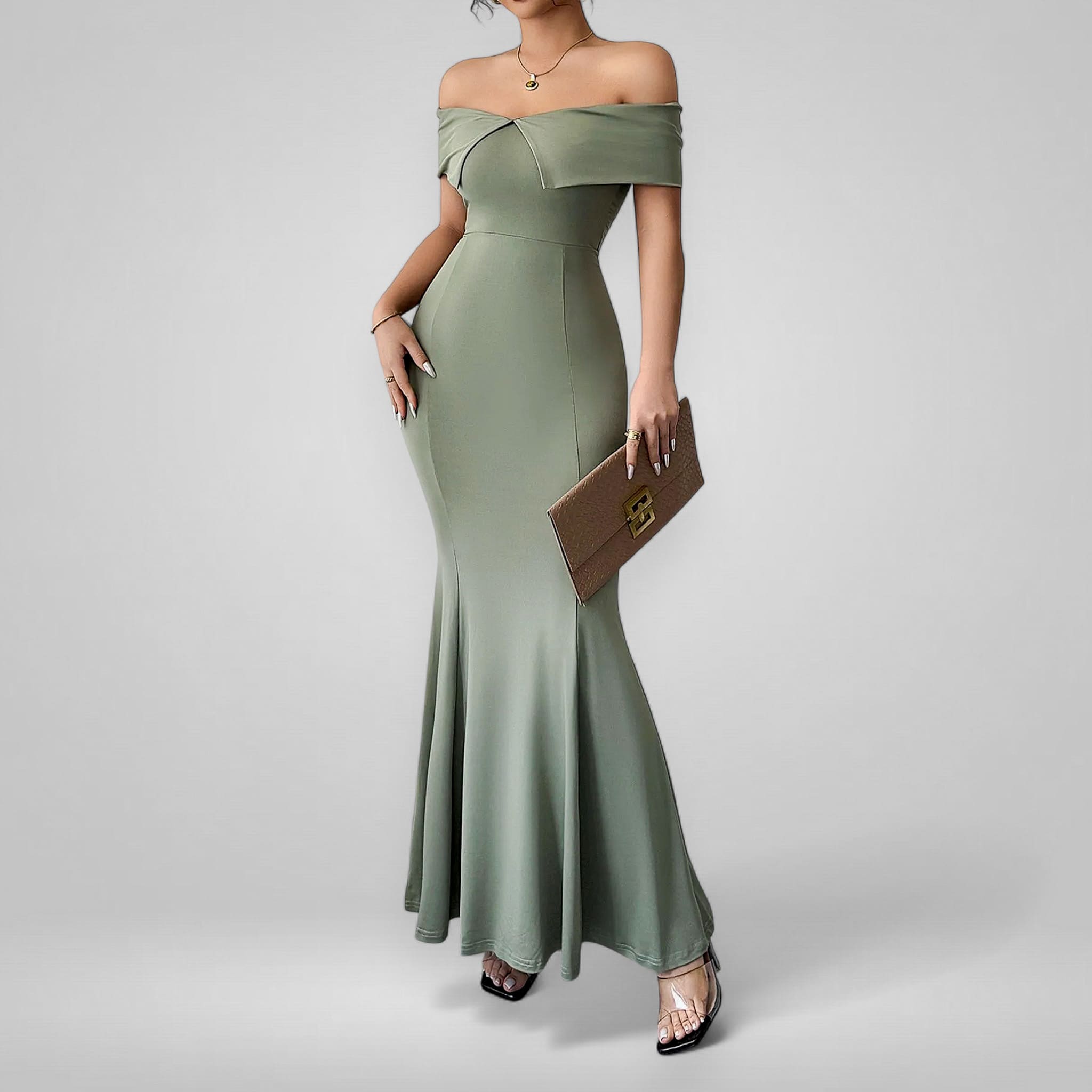 Woman wearing a green off-shoulder gown holding a brown clutch against a gray background
