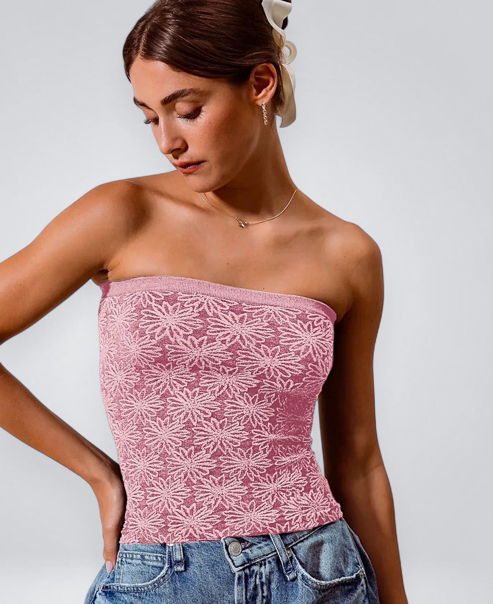 Woman wearing a pink lace strapless top and blue jeans against a plain background